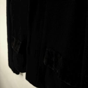 May include: A black blazer with two front pockets. The blazer is made of a textured fabric and has a classic design. The pockets have a velvet-like texture. The blazer is a versatile piece of clothing.