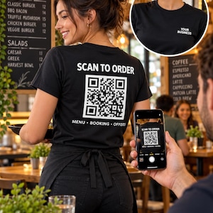 May include: A black short-sleeved t-shirt featuring the white text SCAN TO ORDER above a large QR code and the text MENU • BOOKING • OFFERS below. The front of the shirt displays the text YOUR BUSINESS in white on the upper left chest area.