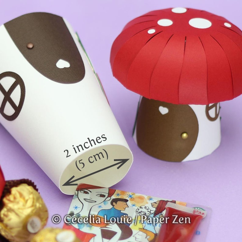 May include: A white paper cone with a brown top and a black circle design. The cone is 2 inches in diameter (5 cm). A red paper mushroom with white polka dots sits next to the cone.