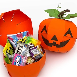 Puede incluir: Caja de golosinas de papel naranja en forma de calabaza con una cara de calabaza. La caja está abierta y llena de caramelos surtidos, incluyendo Nerds, Airheads y chocolate.