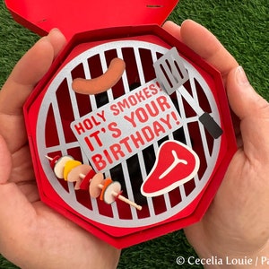 Puede incluir: Una tarjeta de cumplea&ntilde;os en forma de parrilla roja y plateada con el texto "Holy Smokes! It's Your Birthday!" en el interior.