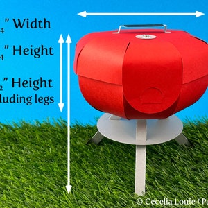 Puede incluir: Barbacoa de papel roja con una base blanca y tres patas. La barbacoa mide 12,1 cm de ancho, 7 cm de alto y 14 cm de alto incluyendo las patas.
