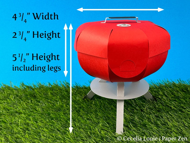 Puede incluir: Barbacoa de papel roja con una base blanca y tres patas. La barbacoa mide 12,1 cm de ancho, 7 cm de alto y 14 cm de alto incluyendo las patas.