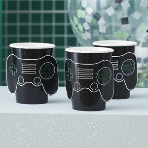 Op de afbeelding: Drie zwarte papieren bekers met een witte omtrek van een videogamecontroller. De controller heeft een plusteken, twee lijnen en een cirkel met vier kleinere cirkels erin.