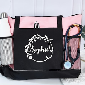 May include: Pink and black tote bag with a white floral design and the name "Sophie". The bag has a mesh side pocket with a white water bottle and another with a stethoscope. The bag is designed for medical professionals.