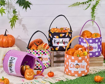 May include: A collection of Halloween-themed treat baskets in various colors and patterns. The baskets are filled with pumpkins and candies. Each basket has a name printed on it, such as "Kristin" and "Charlie".
