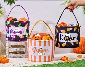 May include: Three Halloween-themed treat bags with handles, filled with pumpkins. One bag is black with a candy and bat pattern, another is orange and white striped, and the third is black with a candy corn pattern. Each bag has a name on it.