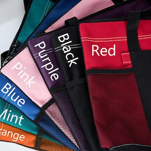 May include: A collection of tote bags in various colors, including red, black, purple, pink, blue, mint, and orange. Each bag has a mesh pocket and a label with the color name in white text.