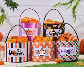 May include: Five Halloween-themed treat baskets filled with pumpkins. Each basket has a different pattern: orange and white stripes, orange polka dots, black and white stripes, black with candy corn, and a colorful polka dot pattern. Each basket has a name on it.
