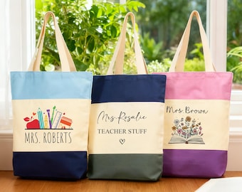 May include: Three canvas tote bags with cream handles and a two-tone design. Each bag features a different colour combination: blue and navy, navy and olive green, and pink and purple. The bags have teacher-themed graphics and names.