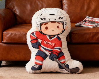 May include: A hockey-themed decorative pillow in the shape of a cartoon hockey player. The player wears a red jersey with the name "MONTY", a white helmet, and blue and white accents. The pillow is on a brown leather couch.