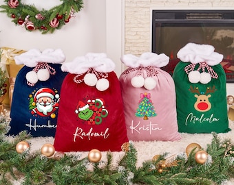 May include: Four plush Christmas gift bags in blue, red, pink, and green, each with a white fluffy top and pom-poms. The bags feature festive designs: Santa Claus, Grinch, Christmas tree, and a reindeer, with personalized names.