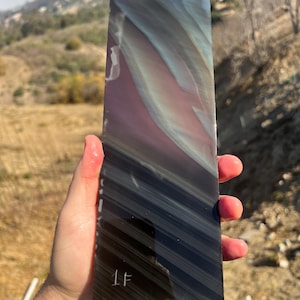 May include: A dark gray obsidian slab with iridescent blue and purple hues. The slab has a striated pattern and is labeled "1F".