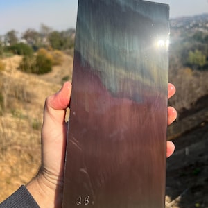 May include: A rectangular piece of metal with a rainbow iridescent finish. The metal has a brushed texture and is marked with the initials "2B".