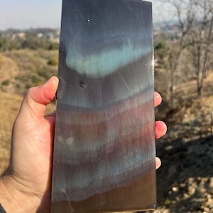 May include: A close-up of a rectangular metal sheet with a blue, green, and brown iridescent finish. The sheet has a smooth, polished surface.