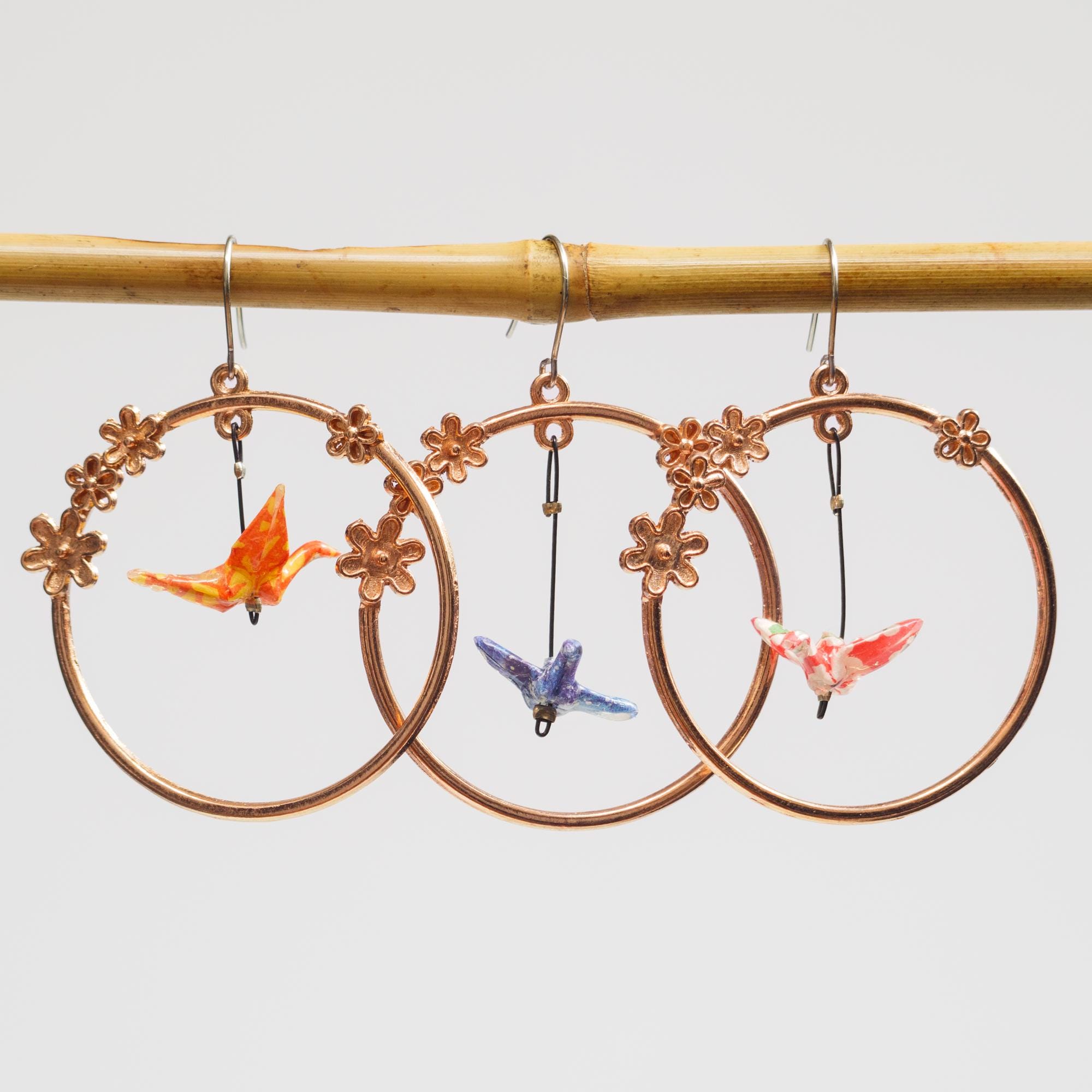 Miniature hand folded Japanese origami paper cranes encased in an ecofriendly varnish seal, dangling within rose gold floral hoop earrings
