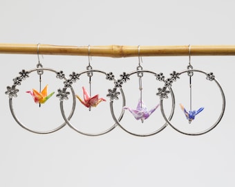 Miniature hand folded Japanese origami paper cranes encased in an ecofriendly varnish seal and dangling within silver floral hoop earrings
