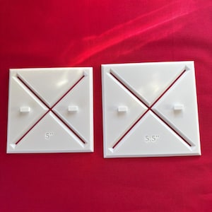 May include: Two white square quilting templates with a red background. One template is labeled "5" and the other is labeled "5.5". Each template has a diagonal design with a small rectangular tab on each side.