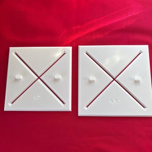 May include: Two white square quilting templates with red accent lines. One template is labeled "6" and the other is labeled "6.5". The templates are on a red background.