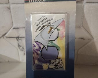 May include: A packaged wallpaper cutting tool with the brand name "ATRON" at the top. The package includes a clear plastic window revealing the tool and a gold screw. Text on the package reads "Cut Your Own Wallpaper" in English and French.