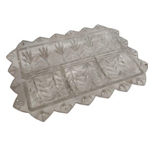 Puede incluir: Fuente de vidrio transparente con tres compartimentos y un patrón decorativo de hojas. La fuente rectangular tiene un borde festoneado. Ideal para servir aperitivos o entremeses.