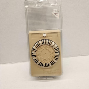 May include: A beige mechanical timer with a circular dial featuring black and white segments. The dial displays numbers indicating hours. The timer has an "OFF" and "ON" switch and is encased in a clear plastic package.