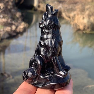 May include: A glossy black wolf figurine in a howling pose. The sculpture is detailed, with visible fur texture and a raised head. The figurine is approximately 4 inches tall.