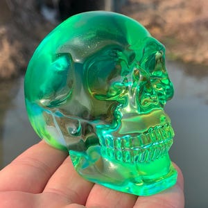Puede incluir: Una escultura de calavera de vidrio verde. La calavera es translúcida y tiene un acabado brillante.