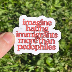 Op de afbeelding: Een witte sticker met rode tekst die luidt: "stel je voor dat je immigranten meer haat dan pedofielen." De sticker wordt tegen een achtergrond van groen gras gehouden.