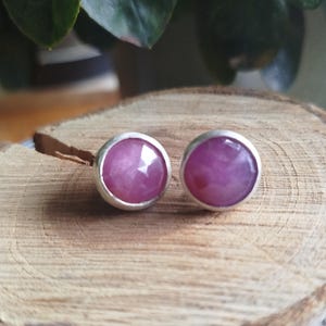 Può includere: Un paio di orecchini a bottone in argento con accenti di pietre preziose rosa. Gli orecchini sono rotondi e hanno una finitura liscia e lucida.