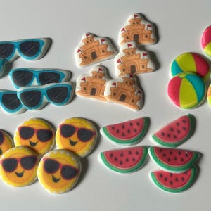 May include: A collection of summer-themed decorations, including sunglasses, smiling suns, sandcastles, watermelon slices, and beach balls. The decorations are in bright colors, perfect for a summer party or event.