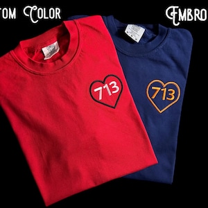 May include: Two crew neck t-shirts, one red and one navy blue, with embroidered heart-shaped designs. The hearts feature the number "713". The text "CUSTOM COLOR" and "EMBROIDERY" are above the shirts.