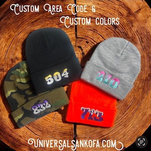 May include: Four knit beanies with different area codes embroidered on them. The beanies are in various colors, including black, gray, camouflage, and orange. The area codes are 504, 210, 832, and 713.