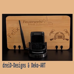Könnte beinhalten: Eine Holzplakette mit dem Text "Feuerwehr Stadt Schwandorf" und einer Feuerwehrhelmgrafik. Die Plakette hat ein schwarzes Funkgerät mit einer Antenne und den Namen "Felix" eingraviert.