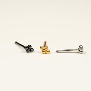 May include: Three nose rings with a cluster of four small balls. The rings are silver, gold, and black.