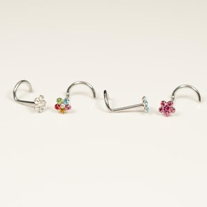 May include: Four silver nose rings with flower-shaped crystal accents. The flowers are in different colors, including pink, blue, white, and rainbow.