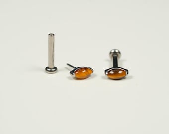 Puede incluir: Tres piezas de joyería corporal de plata con una piedra de ojo de tigre marrón. Las piezas son un pendiente de labio, una barra y una barra recta.