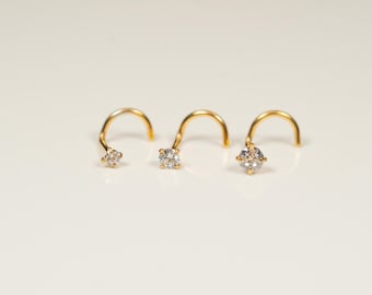Puede incluir: Tres anillos de nariz de oro con una pequeña piedra preciosa transparente en cada uno. Los anillos son curvos y tienen un pequeño bucle en el extremo.