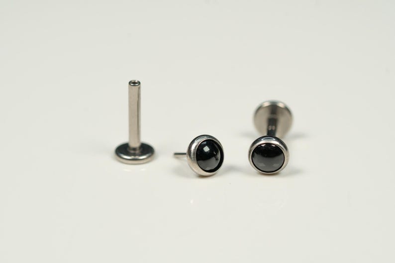 Pu&ograve; includere: Tre pezzi di gioielleria per il corpo argentati con accenti di pietre preziose nere. I pezzi sono un perno labret, una barra e un perno a schiena piatta.