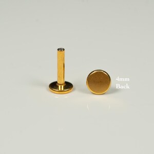 Puede incluir: Joyer&iacute;a corporal dorada con un respaldo de 4 mm. La joyer&iacute;a es un disco plano con una superficie lisa.