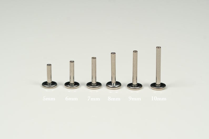 Pu&ograve; includere: Un set di sei barbell in acciaio inox di diverse lunghezze, che vanno da 5 mm a 10 mm. I barbell sono esposti su una superficie bianca.