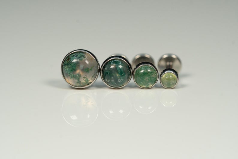 May include: Set of five silver body jewelry pieces with green and white agate stones. The stones are round and have a domed shape. The jewelry is arranged in order of size, with the largest stone on the left and the smallest stone on the right.
