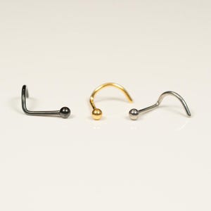 May include: Three nose rings with a ball end. The rings are made of silver, gold, and black metal.