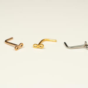 May include: Three nose rings with infinity symbol designs. Two are gold and one is silver.