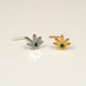 May include: Two nose rings with a green gemstone in the centre. One ring is silver and the other is gold. Both rings are shaped like a marijuana leaf.