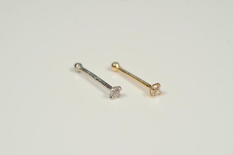 Puede incluir: Dos anillos de nariz con una peque&ntilde;a piedra preciosa transparente en cada uno. Un anillo es de plata y el otro es de oro.