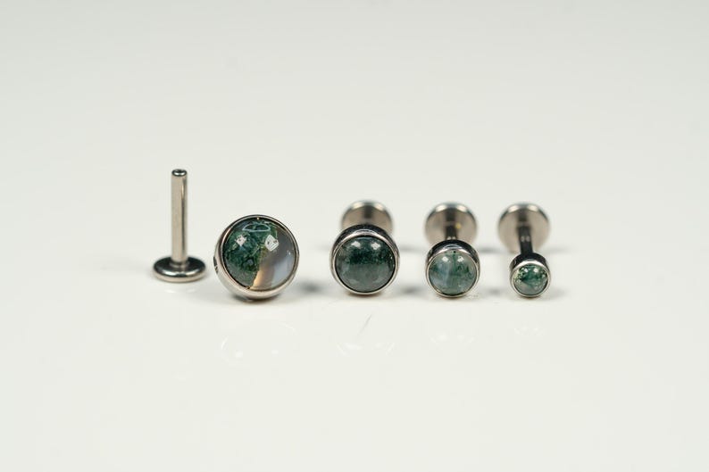 May include: Set of five silver body jewelry pieces with green and white agate stone accents. The jewelry pieces are different sizes and are arranged in a row on a white surface.