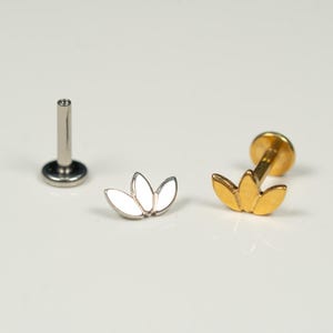 May include: Two different styles of body jewelry, both featuring a lotus flower design. One is gold and the other is silver.