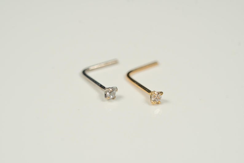 Puede incluir: Dos anillos de nariz con una peque&ntilde;a piedra preciosa transparente. Un anillo es de plata y el otro es de oro.
