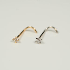 Puede incluir: Dos anillos de nariz con un peque&ntilde;o diamante engastado en garras. El anillo de nariz de la izquierda es de oro y el anillo de nariz de la derecha es de plata.